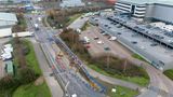 Drone image of an area of road which is under construction. Next to the construction is a car park with parked cars and lorries.  