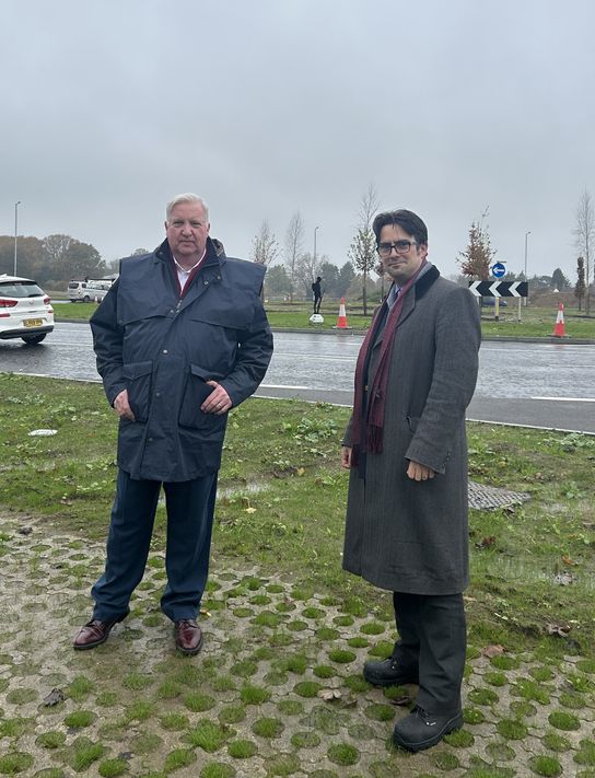 Two men are standing next to each other. Between them, in the distance, you can see an Unknown Tommy Statue.