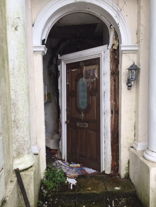 Derelict front entrance to a property in Folkestone. Door is ajar and rubbish can be seen in the porchway