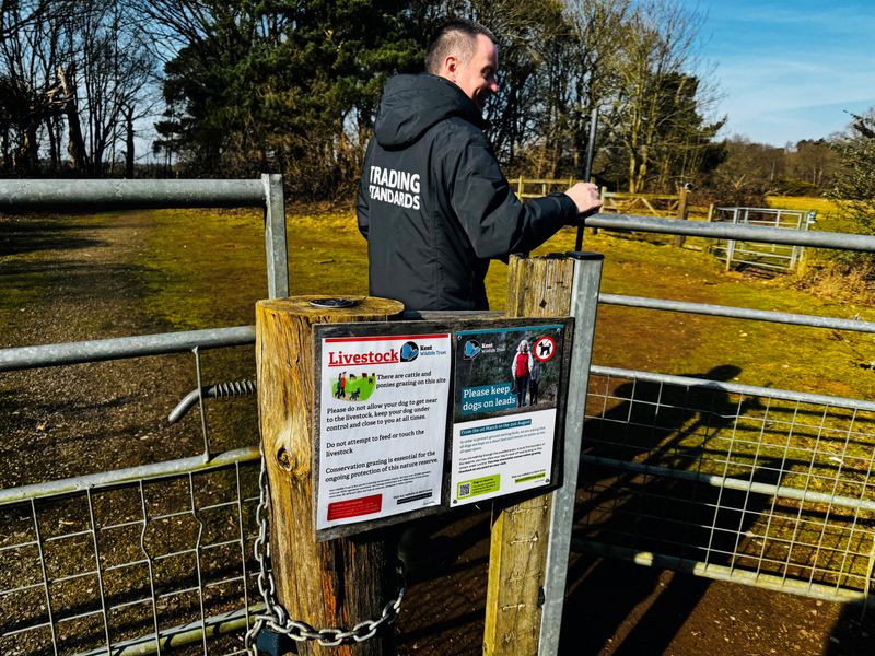 A Trading Standards officer goes through a gate in the country that has advice for dog owners on it about keeping pets on a lead around livestock