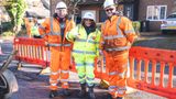 Council leader Linden Kemkaran standing on top of a pothole she has repair in bright yellow PPE and a hard hat. She is pointing down at the repaired road standing next to two highways engineers wearing orange PPE and hard hats