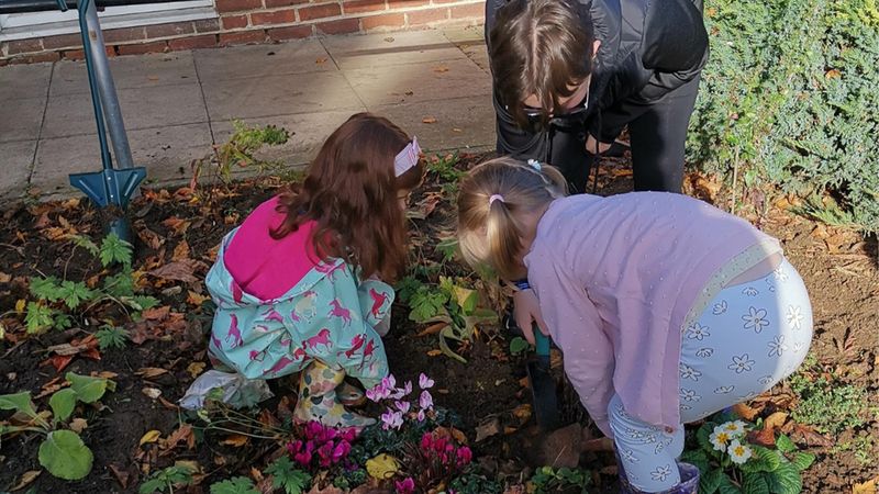 Young children crouching down to plant bulbs in the garden 