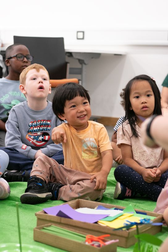 Children take part in a library activity session, sitting on a mat and engaging with a group leader during a Summer Reading Challenge event.