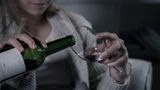 Woman sat alone on sofa pours herself a glass of wine 