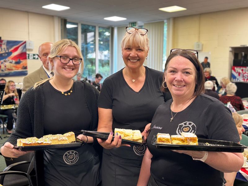 Three caterers hold up homemade traybake cakes served at the Victory in Europe 80th anniversary event in Aylesford