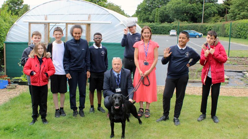Pupils in uniform standing in the garden at Broomhill Bank School with teachers, including Executive Headteacher Steve Ackerley, and a black dog. 