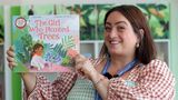 A staff member from Newington Library holding up a book called "The Girl Who Planted Trees" and smiling 