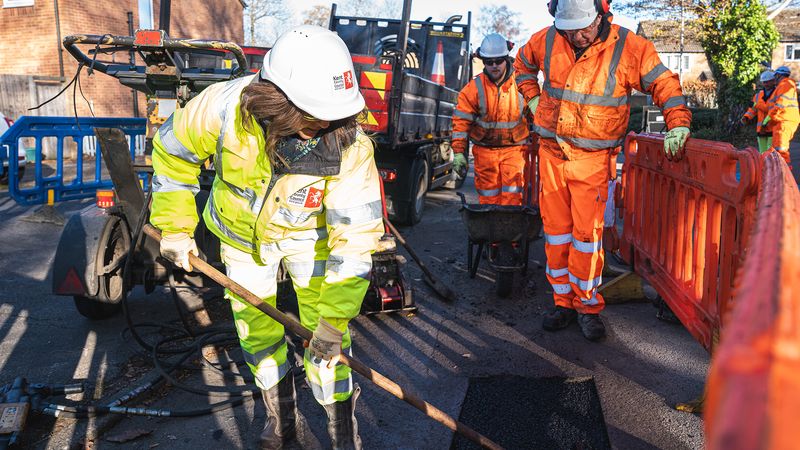 KCC leader wearing yellow hi-vis safety gear and a hard hat leaning over to repair a pothole