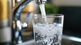 Water from a chrome kitchen tap being poured into a glass 
