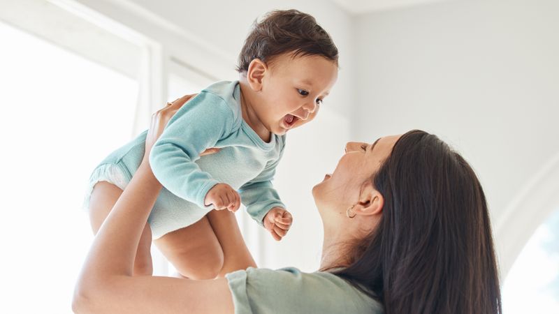 A young baby laughs as his mum lifts him up in the air