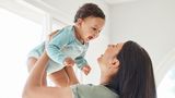 A young baby laughs as his mum lifts him up in the air