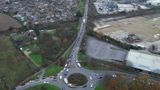 The image shows a road with a roundabout in an urban brownfield area with cars queuing