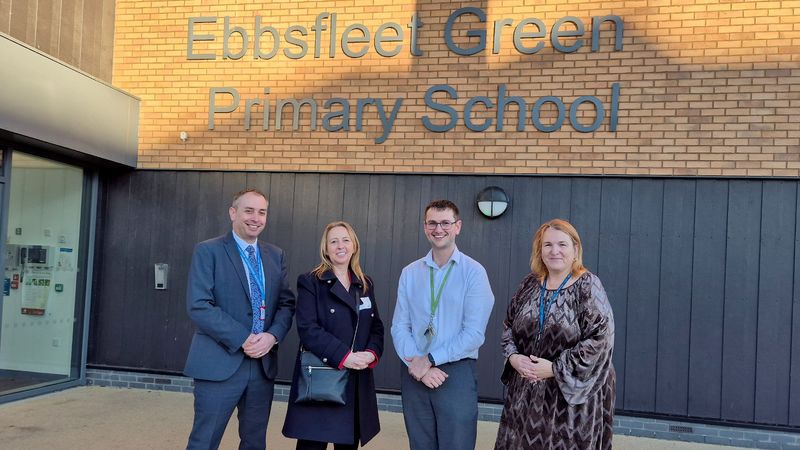 Four representatives from KCC and Ebbsfleet Green Primary School standing outside a brick wall at the schools main entrance with the school sign on the wall in the background