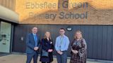 Four representatives from KCC and Ebbsfleet Green Primary School standing outside a brick wall at the schools main entrance with the school sign on the wall in the background