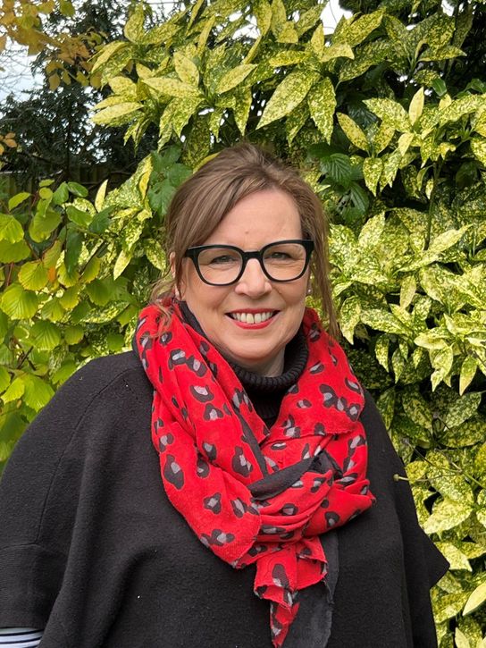 Person wearing a red scarf, standing in front of green shrub