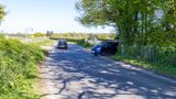 A photograph of a road with a car driving along it and at the junction a van is trying to come out.
