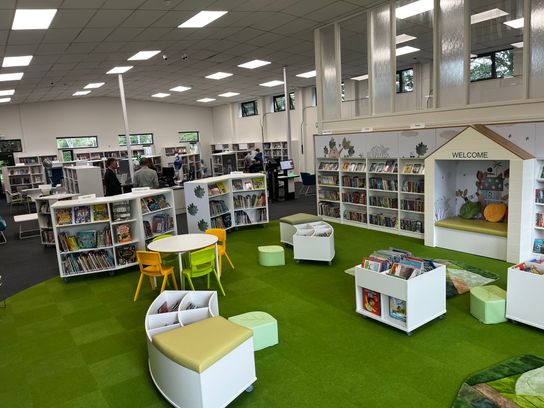 The inside of a library - there are books and a green carpet and chairs.