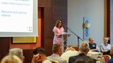 A woman stands at a podium speaking to a group of people.