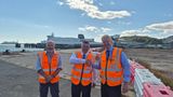 Toby Howe with Peter Osborne and Doug Bannister wearing orange high-visibility vests with two shaking hands. A DFDS ferry, port infrastructure and the white cliffs of Dover are visible in the background.