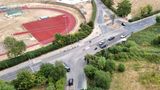 Aerial view of the Badsell Road junction in Paddock Wood, showing the signal-controlled intersection, pedestrian crossing points and several vehicles using the junction. An athletics track is visible to the left, with open land and vegetation surrounding the roads.