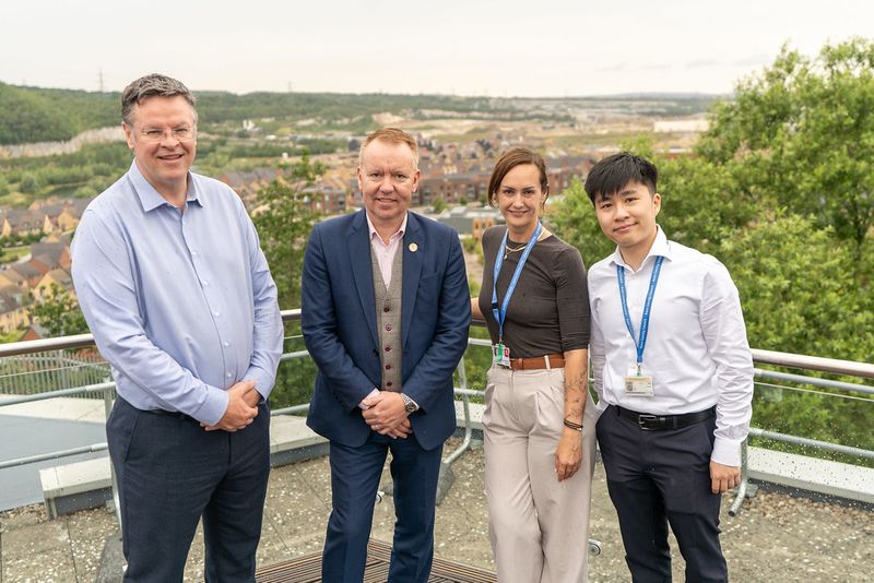 Four people standing on an outdoor viewing platform overlooking a large housing development and surrounding landscape.