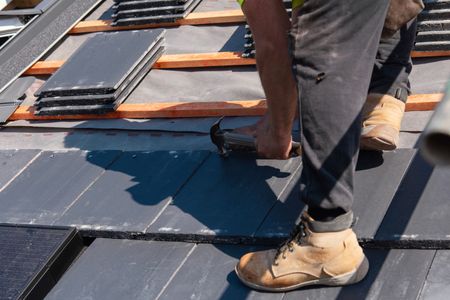 A roofer fixes slate tiles on a roof