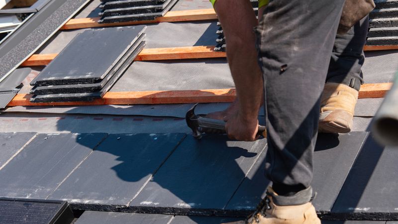 A roofer fixes slate tiles on a roof