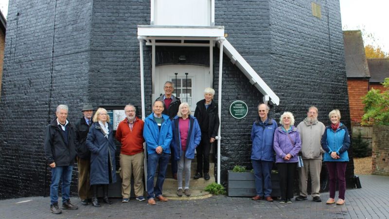 A group of men and women standing outside Cranbrook Windmill smiling at the camera.