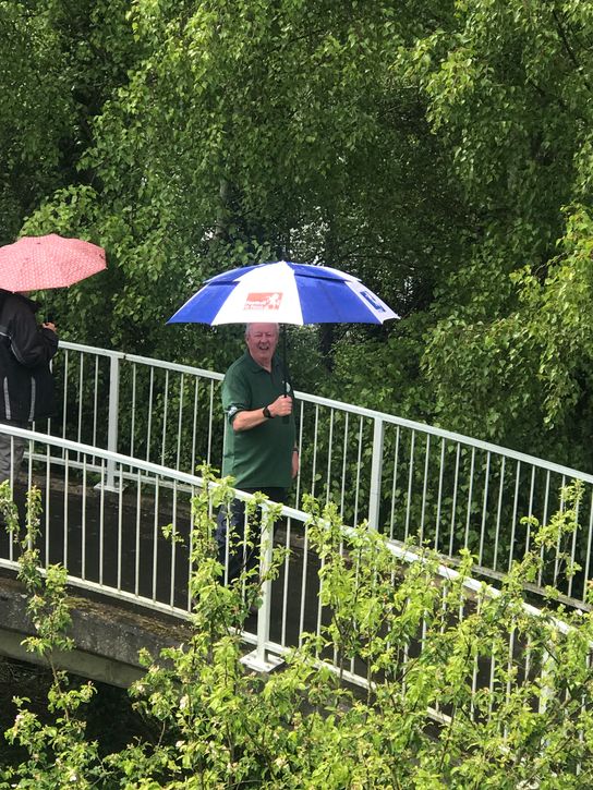 Walk Leader Alex holding an umbrella as he crosses a small railway bridge surrounded by green trees