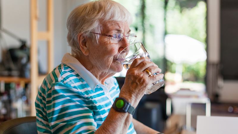 Elderly woman drinks a glass of water in her kitchen