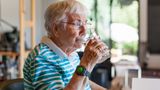 Elderly woman drinks a glass of water in her kitchen