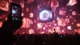 Inside a venue with a crowd of people holding their phones up to capture an immersive light show