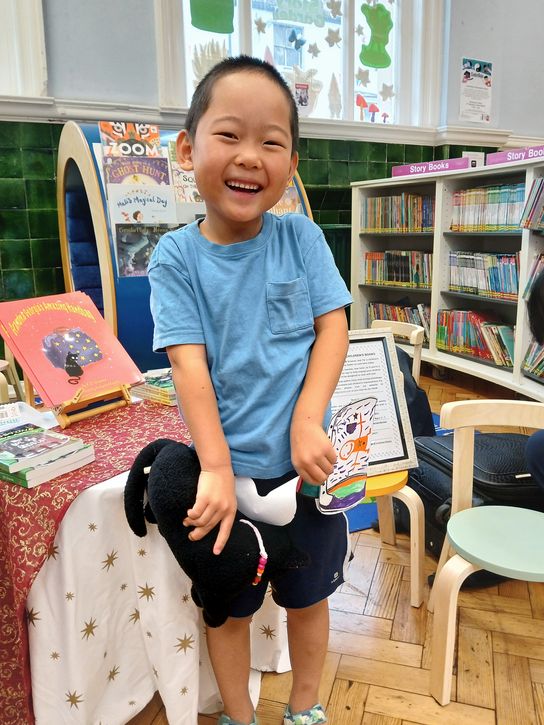 A young boy smiling and holding a teddy in the children's section of Gravesend Library