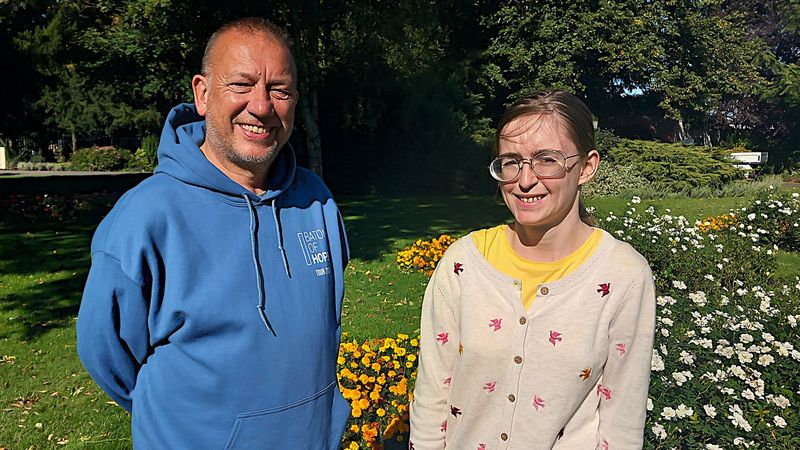 Colin Jones and Kirsten Wood standing together in front of a park flower bed
