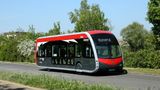 A red, black and grey Fastrack bus travelling on a quiet road lined with greenery, displaying Bluewater A on its destination screen.