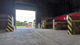 Interior of a waste transfer station showing a newly laid concrete floor, large open vehicle entrance, and reinforced waste bays with black and yellow hazard markings along the walls.