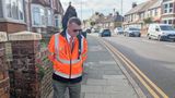 A man wearing an orange hi-viz walks along inspecting  a road.