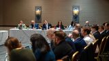 Panel members sit at the front of a conference room during a water partnership meeting, while attendees listen and take part in discussion from tables arranged around the room.