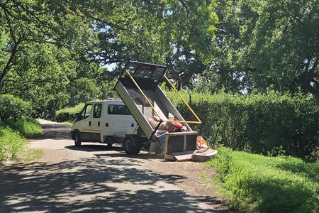 A photo of a truck on a country road fly-tipping lots of waste onto the road.