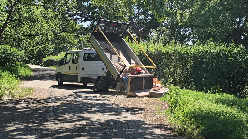 A photo of a truck on a country road fly-tipping lots of waste onto the road.