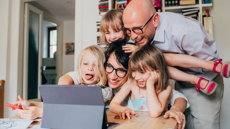 Happy family of a mother and a father infront of a laptop surrounded by their three happy children