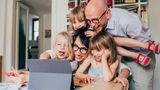 Happy family of a mother and a father infront of a laptop surrounded by their three happy children