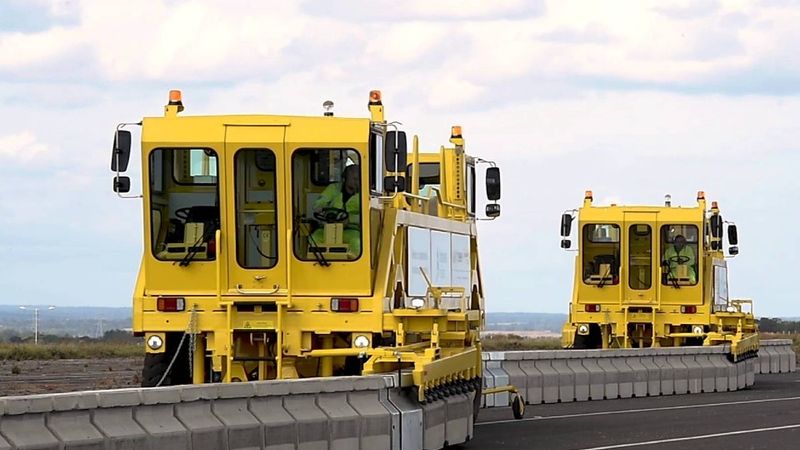 Two large yellow machinery vehicles on the road, placing down stone blocks to support Operation Brock