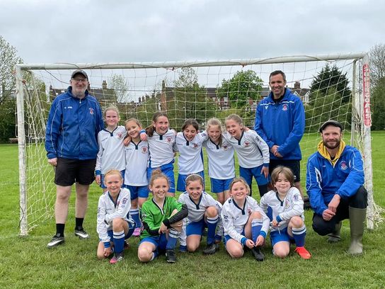 Aaron Hill standing to the left of one of the Tonbridge Junior girls football teams, lined up in front of a net