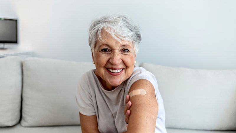 Older woman proudly showing off the plaster on her arm where she has been vaccinated