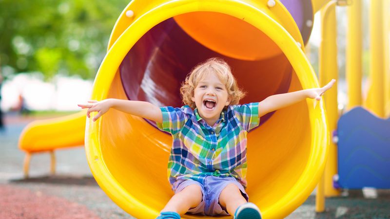 Child on yellow slide in outdoor play area