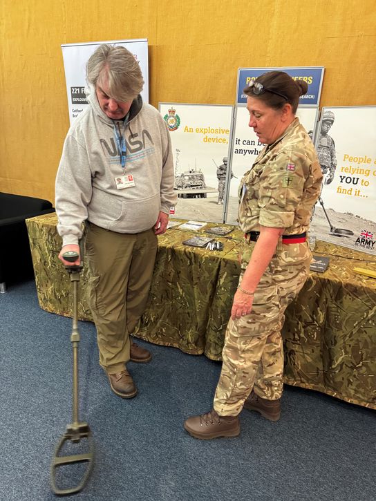 A Royal Engineers reservist in camouflage gear shows a visitor to the reservist and cadets event a piece of equipment