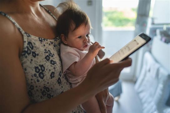 Close up of a baby being held in an adult's arms with that person also holding a digital device