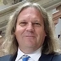 Paul Webb is smiling for his headshot photo in front of the county hall steps