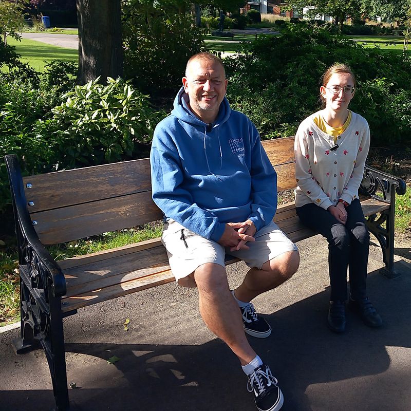 Colin Jones and Kirsten Wood sitting on a park bench on a sunny day
